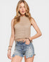 Woman wearing a beige knitted top and denim shorts on a light gray background