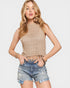 Woman wearing a beige crochet top and denim shorts on a light gray background