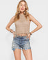 Woman wearing a beige knitted top and denim shorts on a plain background