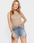 Woman wearing a beige sleeveless top and denim shorts on a white background