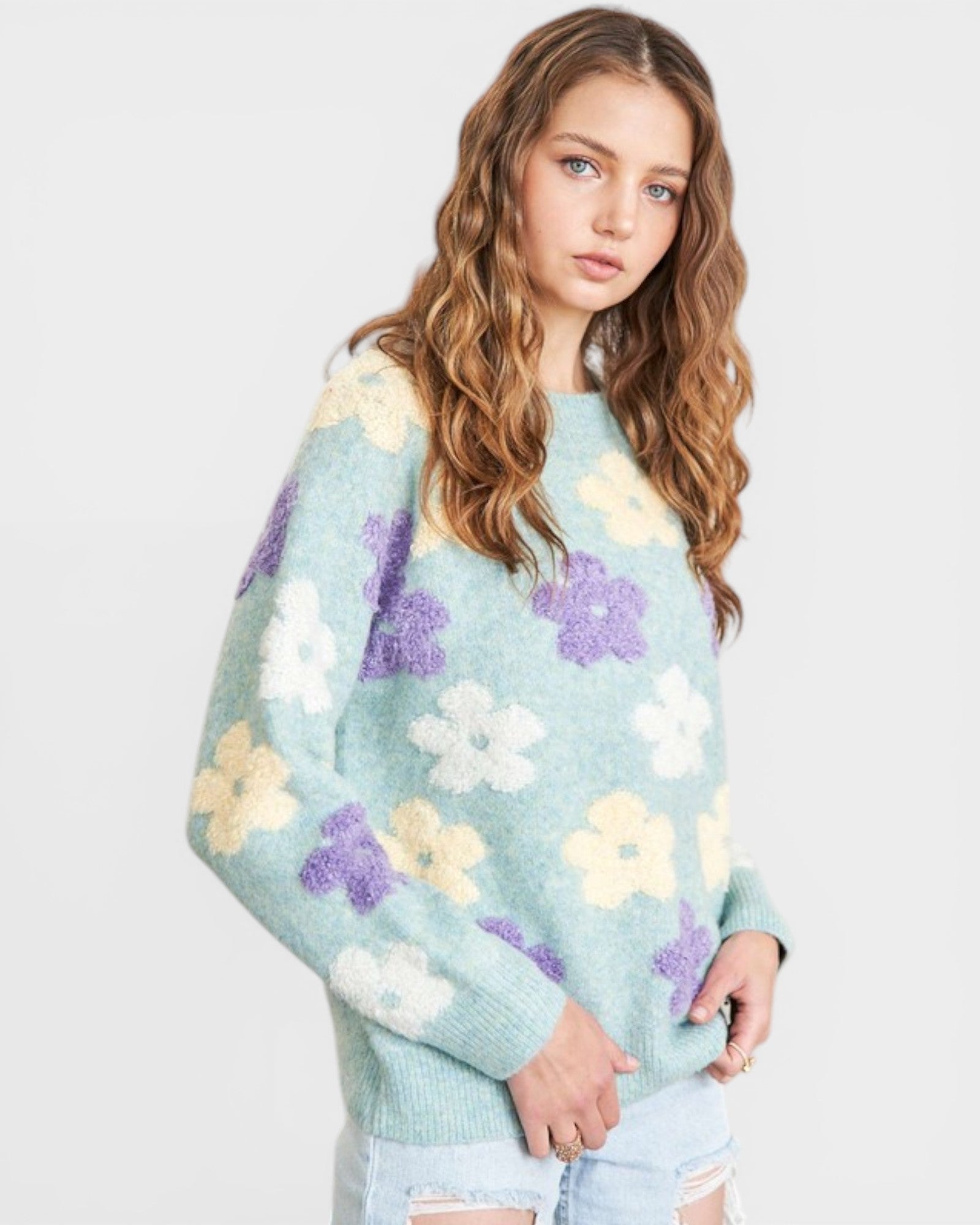 Woman wearing a light blue sweater with floral patterns on a plain background