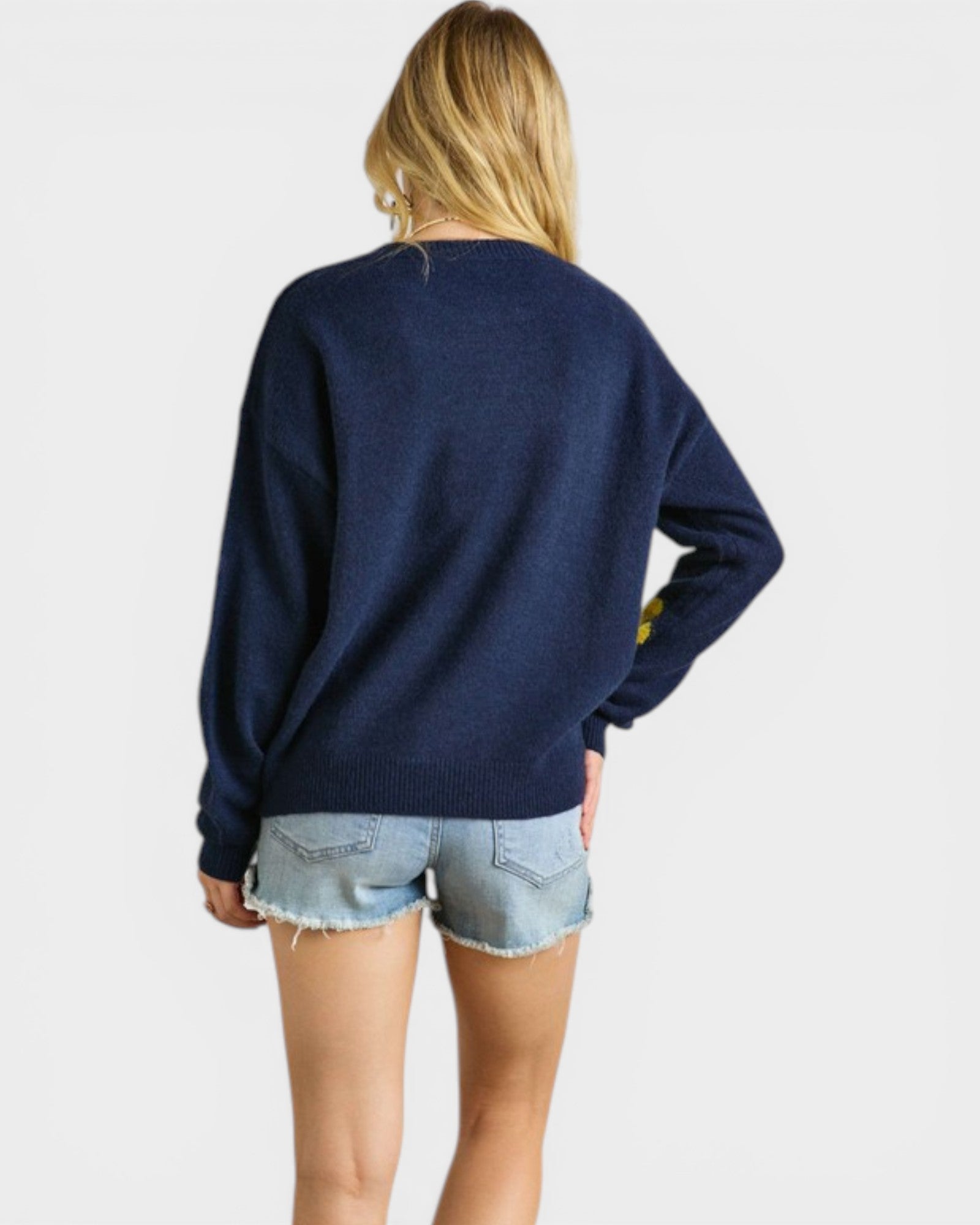 Person wearing a navy sweater and denim shorts on a plain background