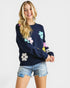 Woman wearing a navy sweater with colorful flower patterns on a white background