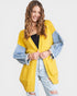 Woman wearing a yellow cardigan with denim sleeves on a white background