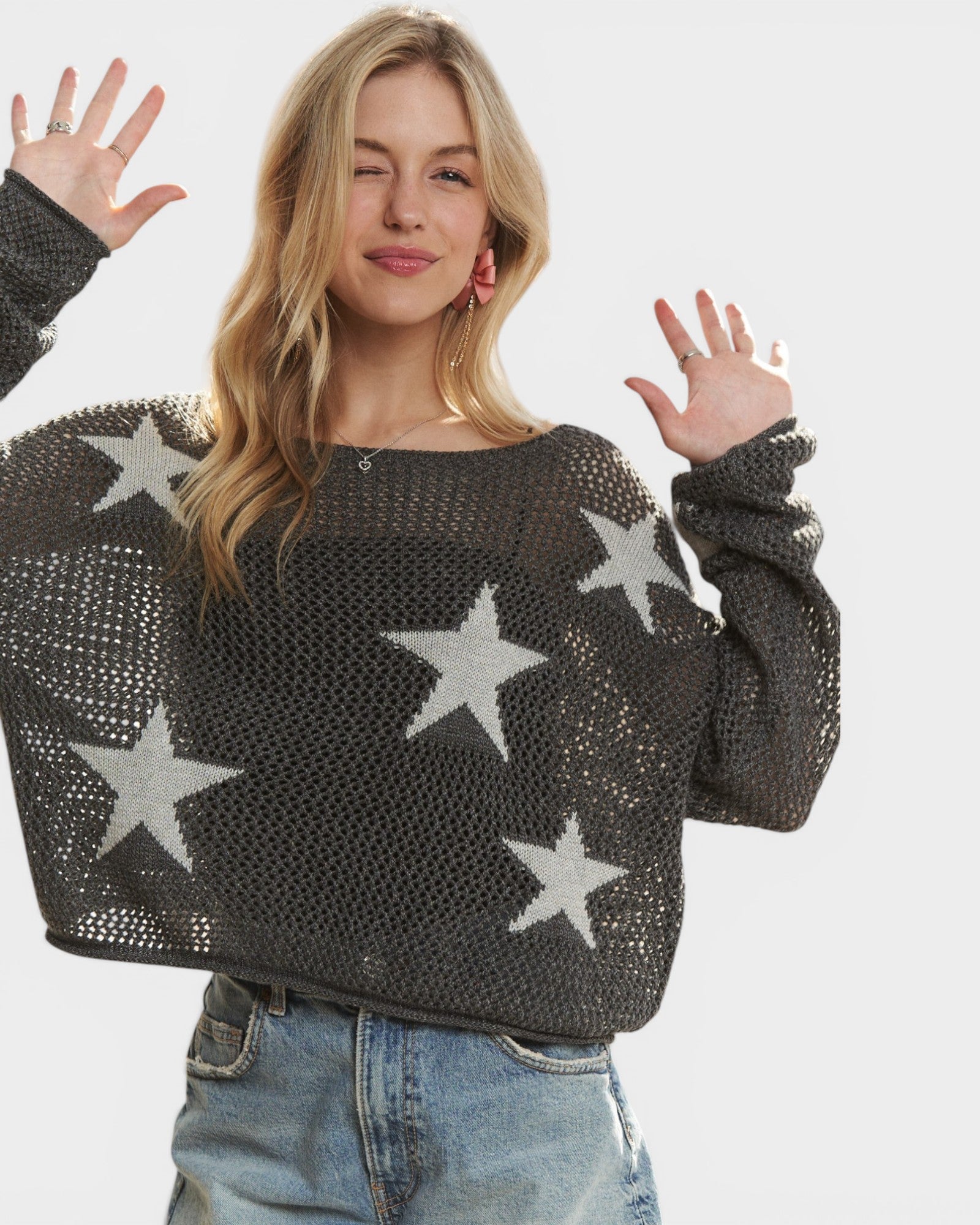 Woman wearing a dark gray sweater with star patterns on a plain background