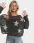 Woman wearing a dark gray sweater with star patterns on a plain background