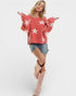 Woman wearing a red sweater with white star patterns, denim shorts, and pink boots on a white background