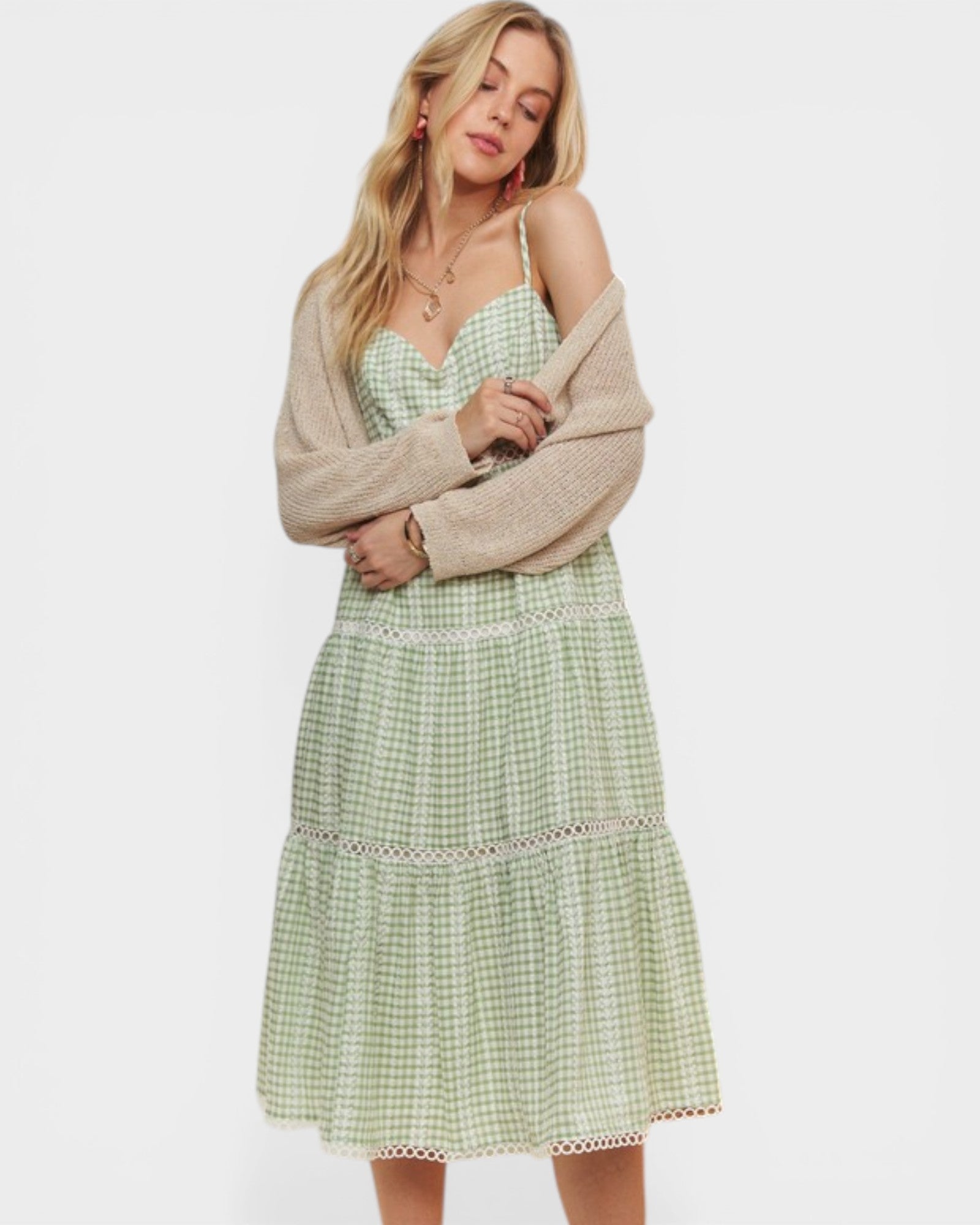 Woman wearing a green checkered dress with a beige cardigan on a white background