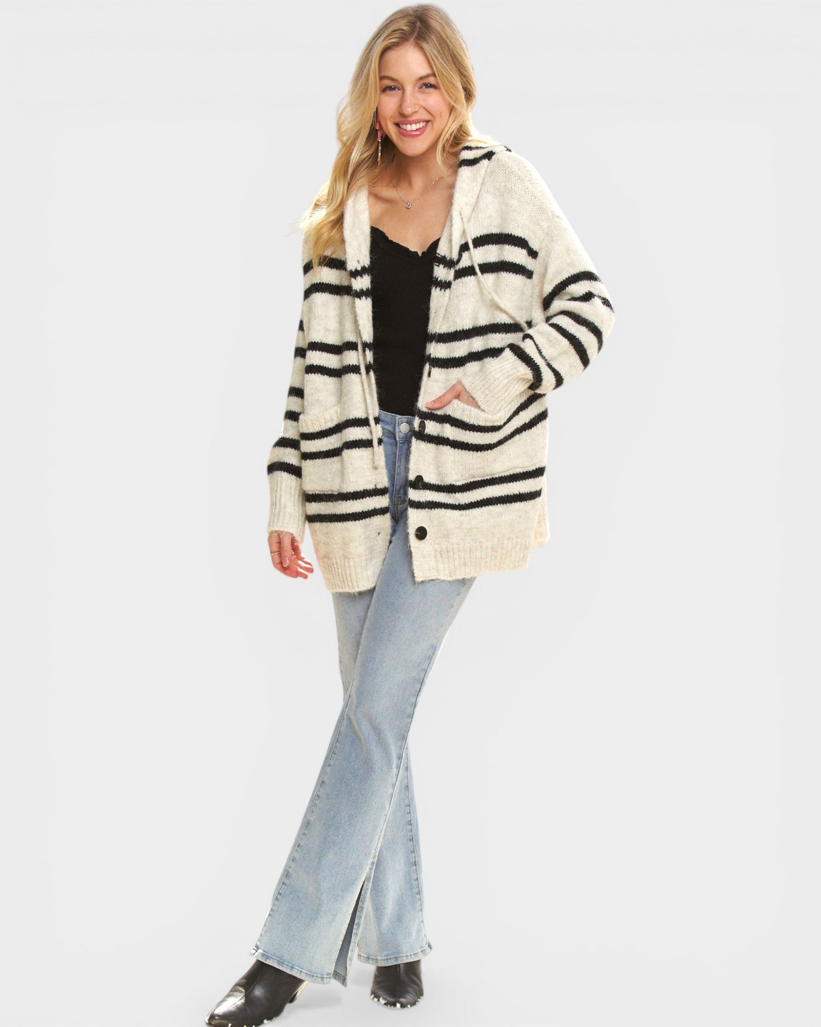 Woman wearing a striped cardigan, black top, and light blue jeans on a white background