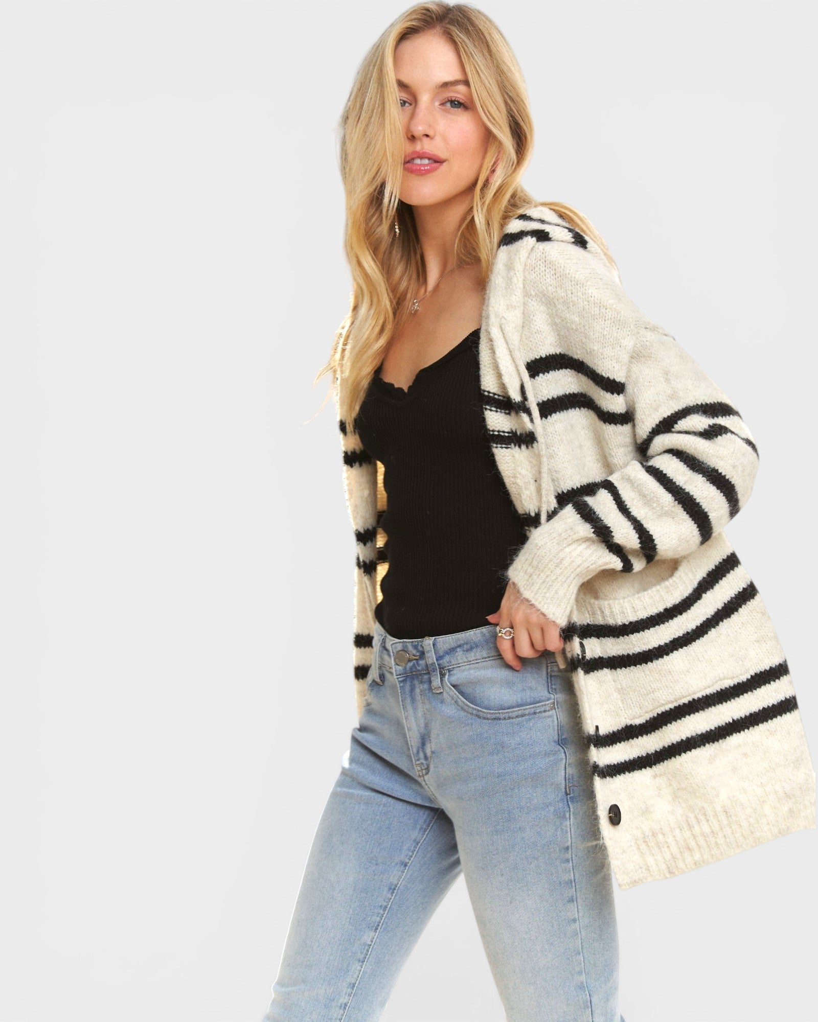 Woman wearing a striped cardigan, black top, and jeans on a light gray background