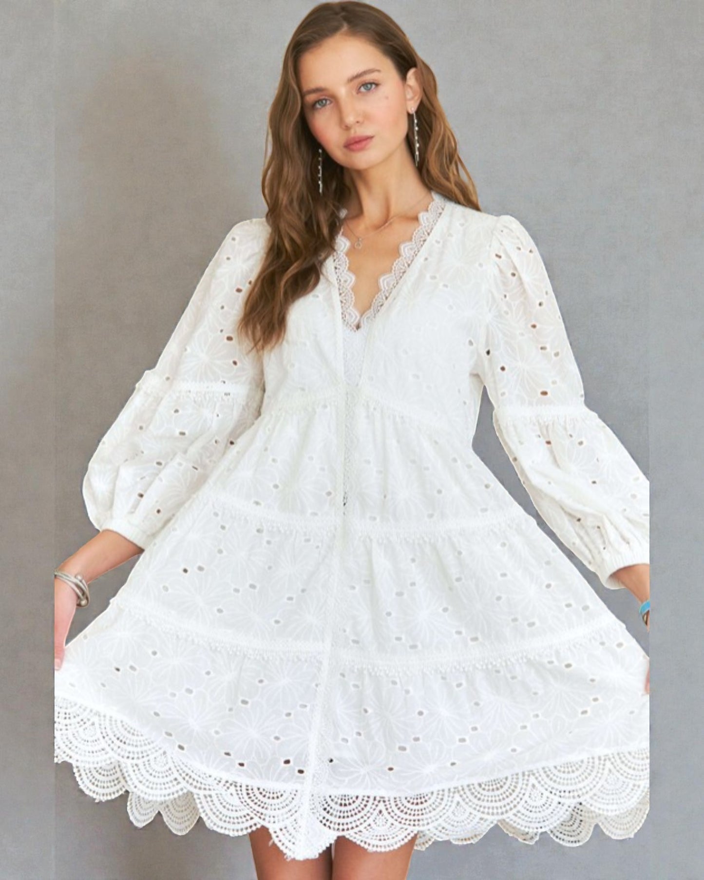 Woman wearing a white dress with long sleeves against a gray background