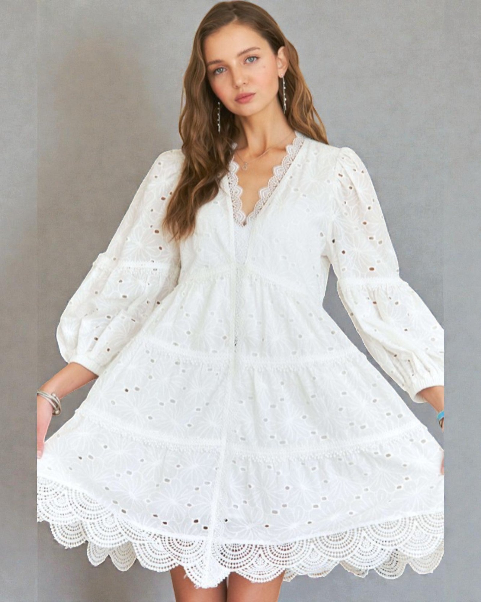 Woman wearing a white dress with long sleeves against a gray background