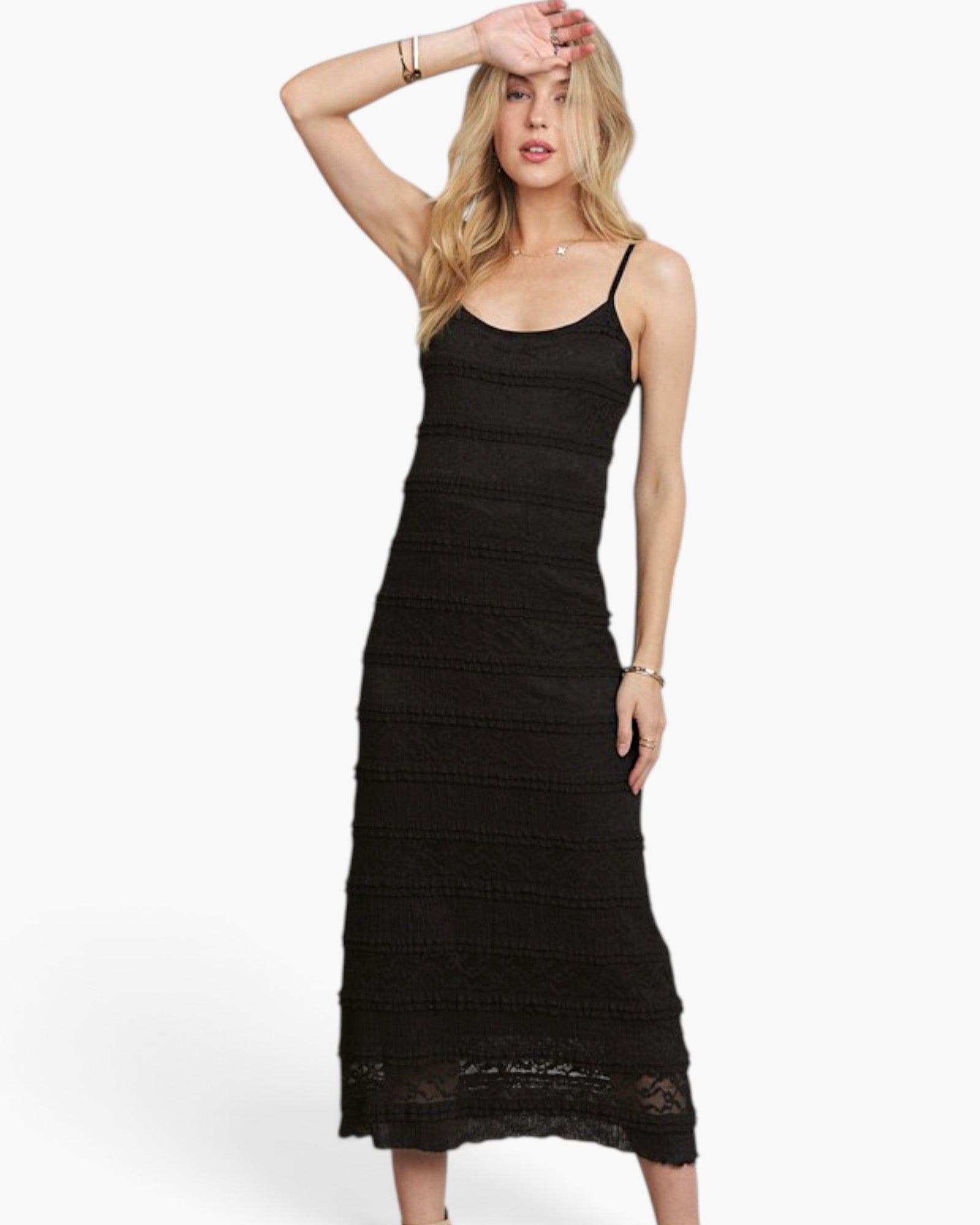 A woman modeling a black sleeveless midi dress with thin straps and a textured, tiered lace-like design against a plain white studio background.