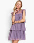 A woman modeling a lavender purple tiered tulle dress with ruffled cap sleeves against a plain white studio background.