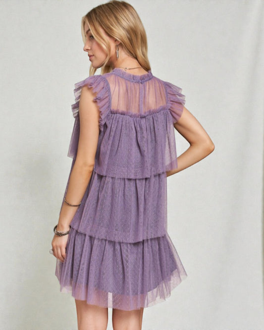 Woman wearing a purple tiered dress against a plain background