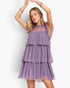 A woman modeling a lavender purple tiered tulle dress with sheer mesh panels and ruffled sleeves, posed against a clean white studio background.