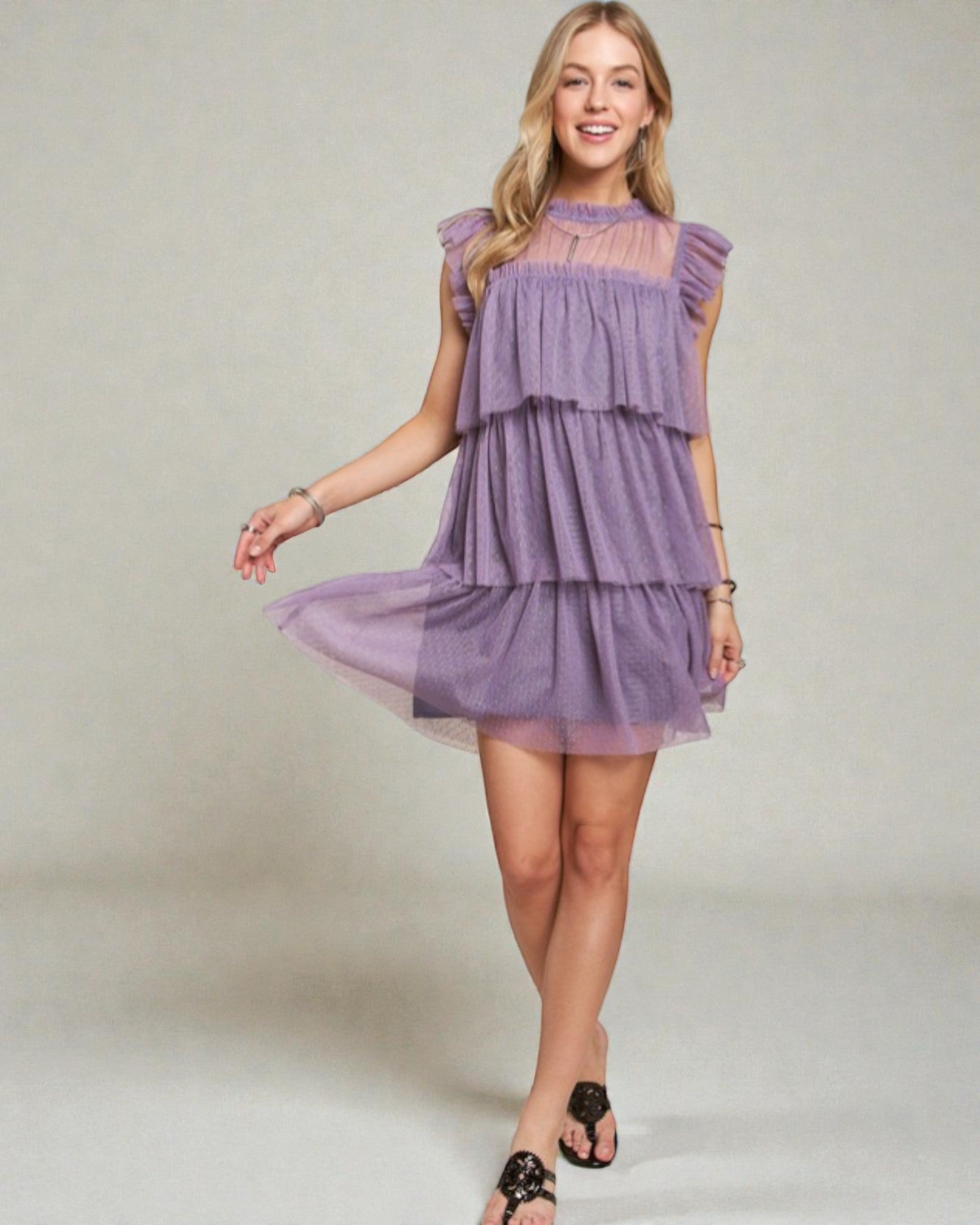 Woman wearing a purple tiered dress on a plain background