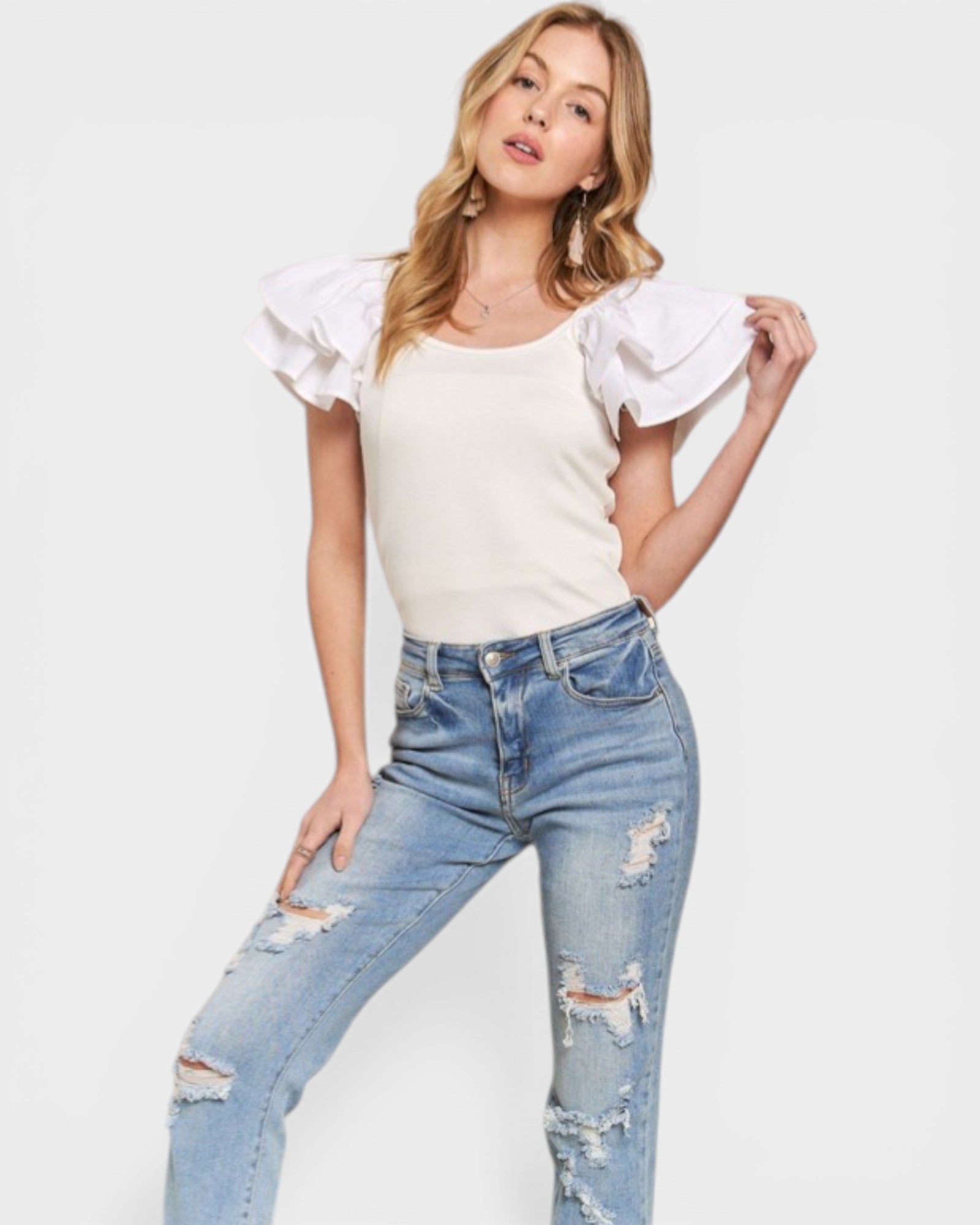Woman wearing a white top with ruffled sleeves and distressed jeans on a white background