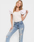 Woman wearing a white top with ruffled sleeves and distressed jeans on a white background