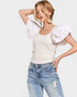 Woman wearing a white top with ruffled sleeves and blue jeans on a light gray background