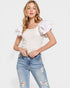 Woman wearing a white top with ruffled sleeves and ripped jeans on a white background