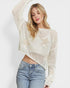 Woman wearing a white knit sweater with star patterns and blue jeans on a light background