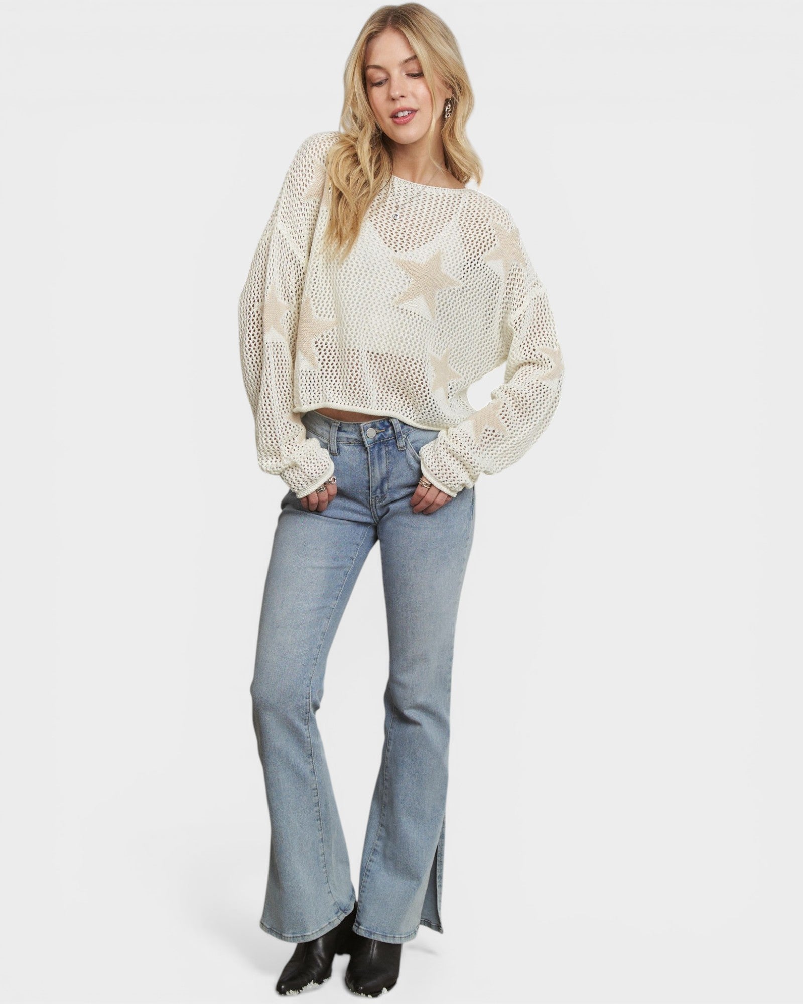 Woman wearing a white perforated sweater and light blue jeans on a white background
