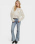 Woman wearing a white perforated sweater and light blue jeans on a white background