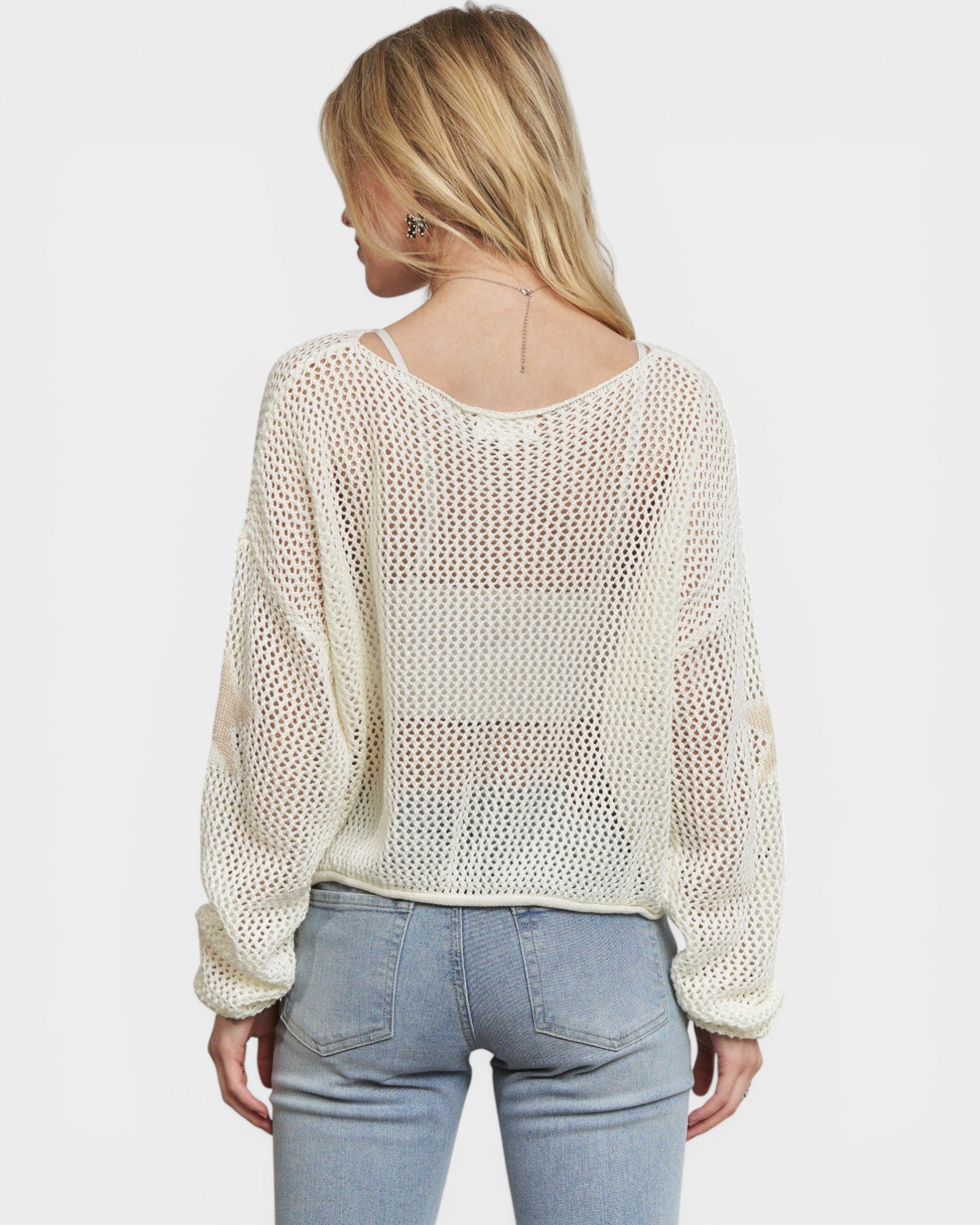 Woman wearing a beige mesh top and light blue jeans on a white background