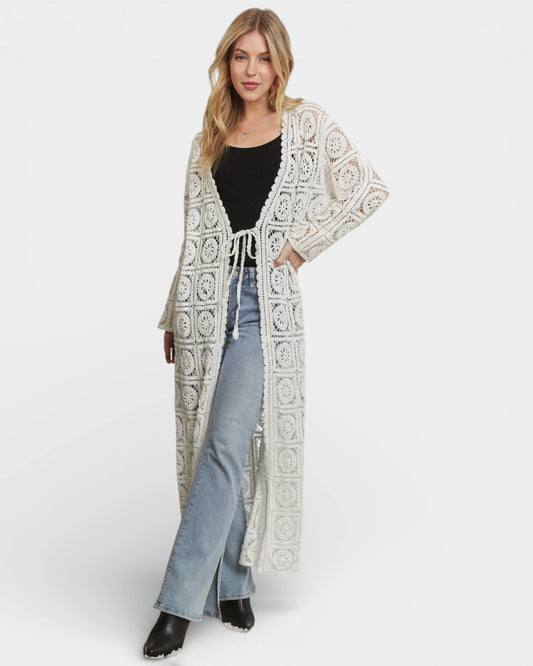 Woman wearing a long, patterned cardigan over a black top and jeans on a white background