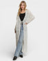 Woman wearing a long, patterned cardigan over a black top and jeans on a white background