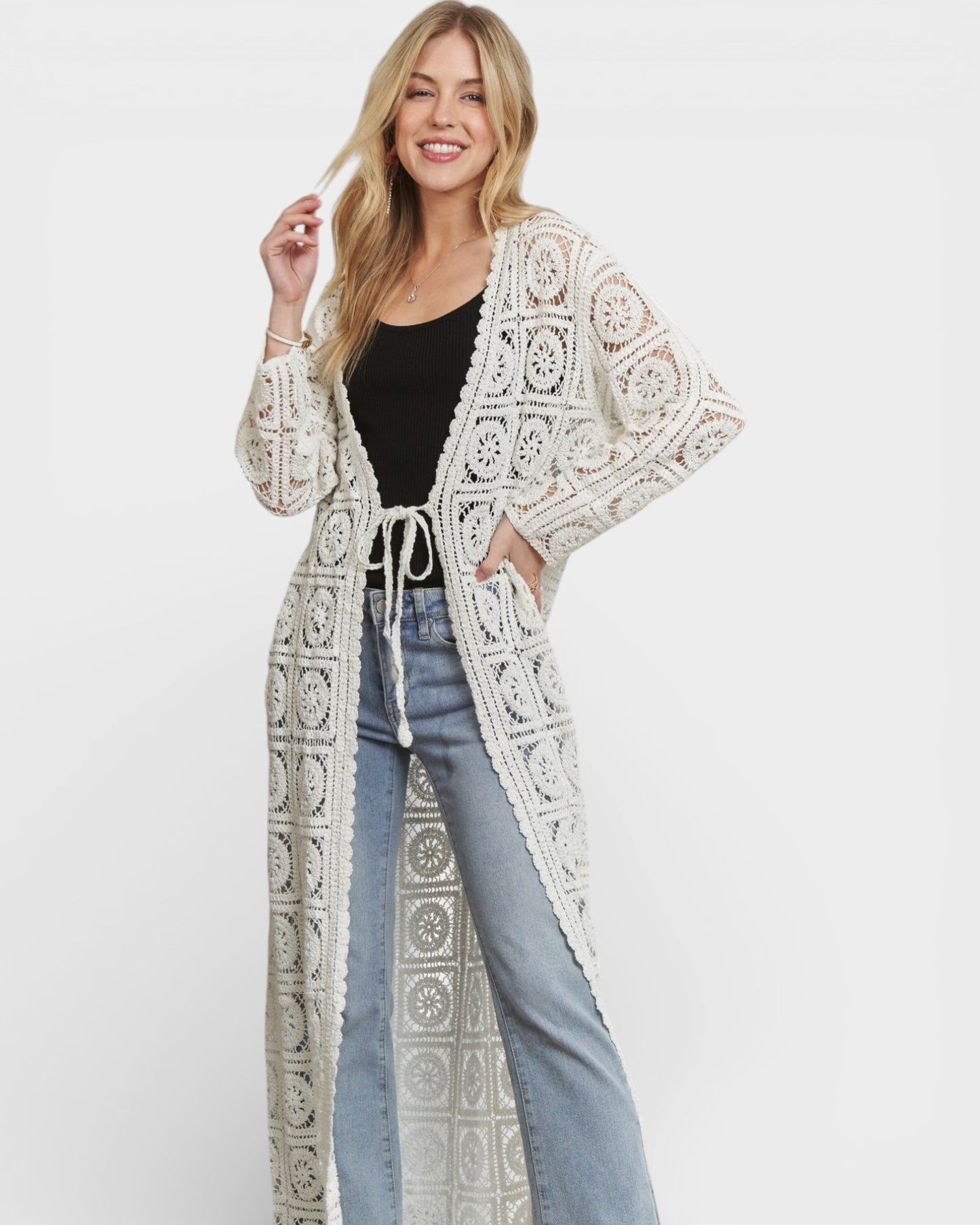 Woman wearing a long, patterned white cardigan over a black top and blue jeans on a white background