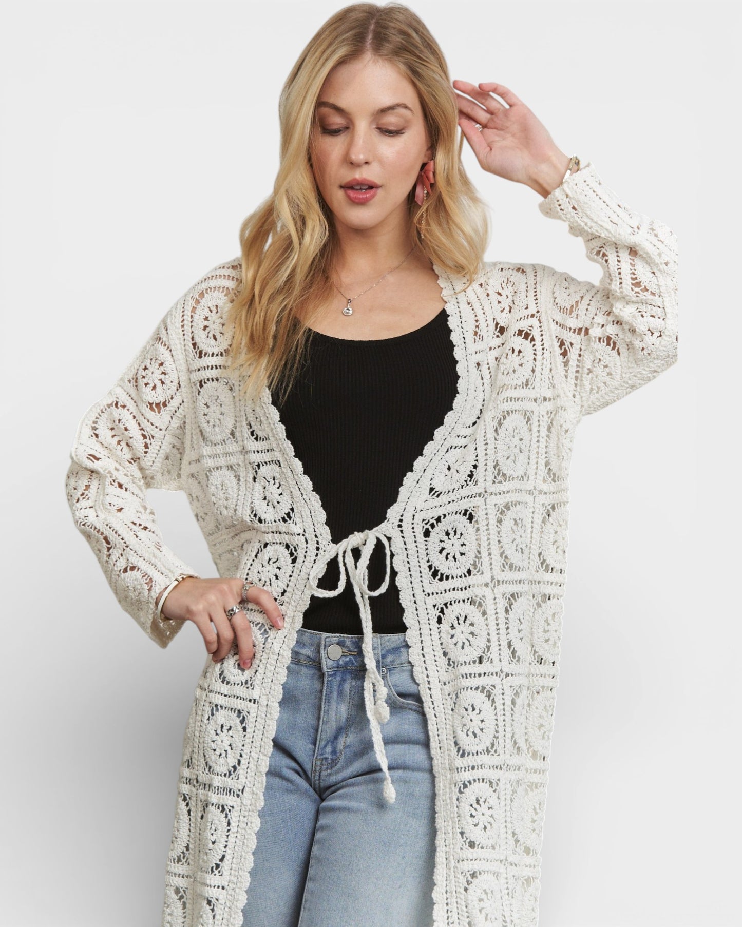 Woman wearing a white crochet cardigan over a black top and blue jeans on a white background