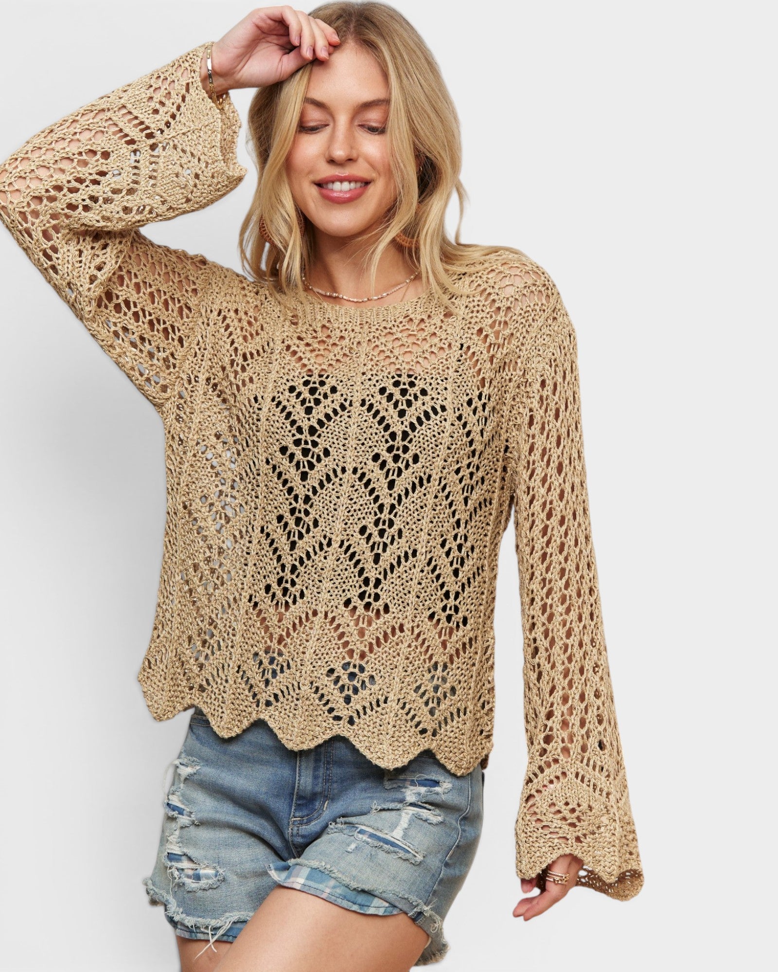 Woman wearing a beige crochet sweater and denim shorts on a white background