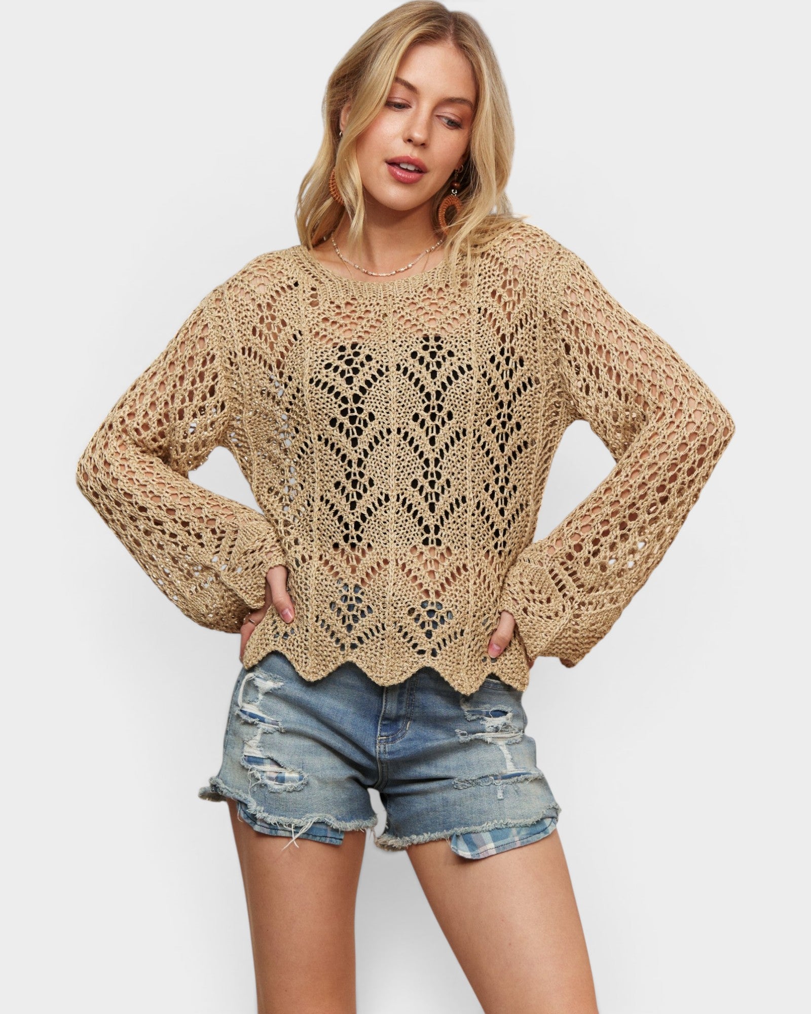 Woman wearing a beige crochet sweater and denim shorts on a white background