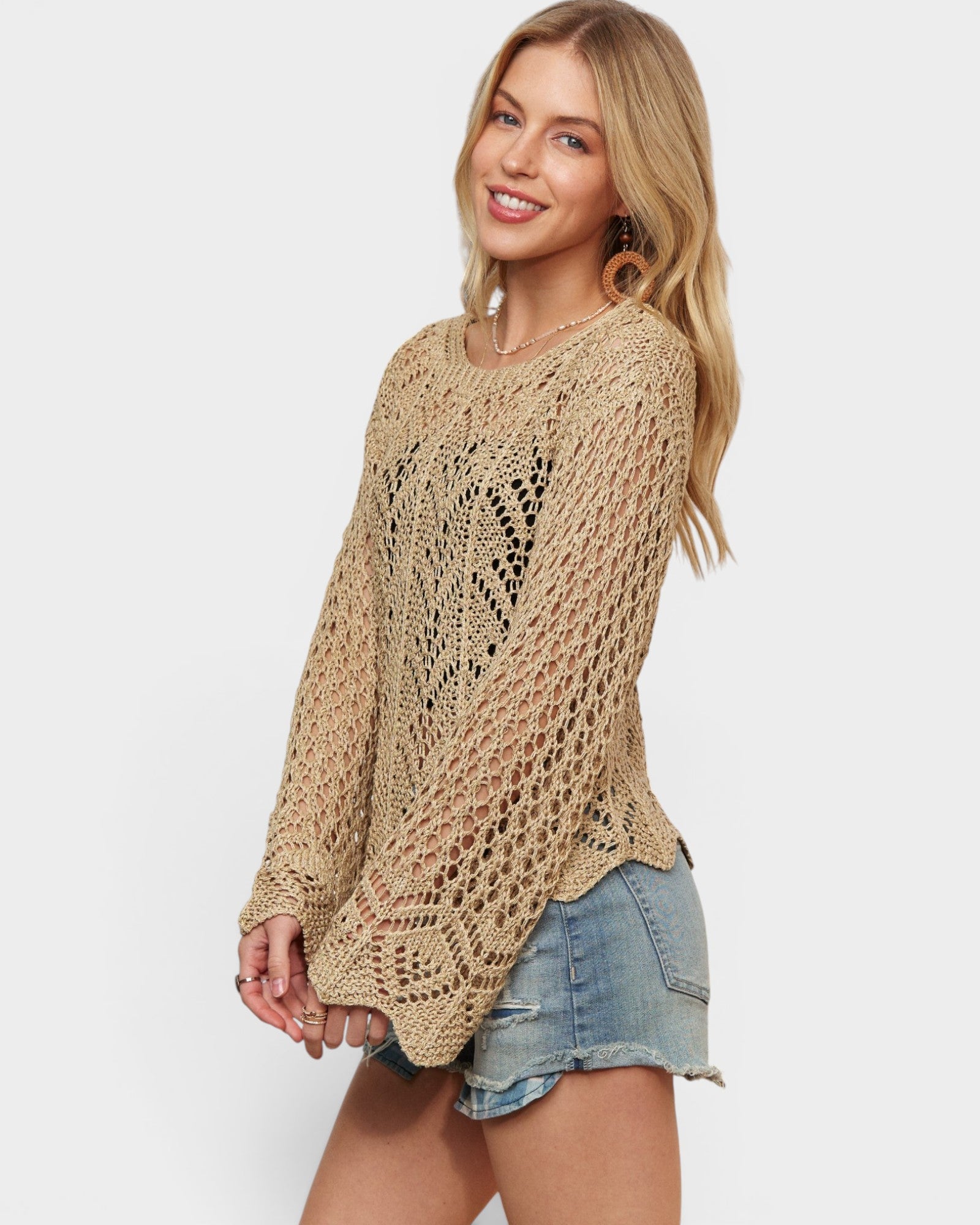 Woman wearing a beige crochet sweater and denim shorts on a white background