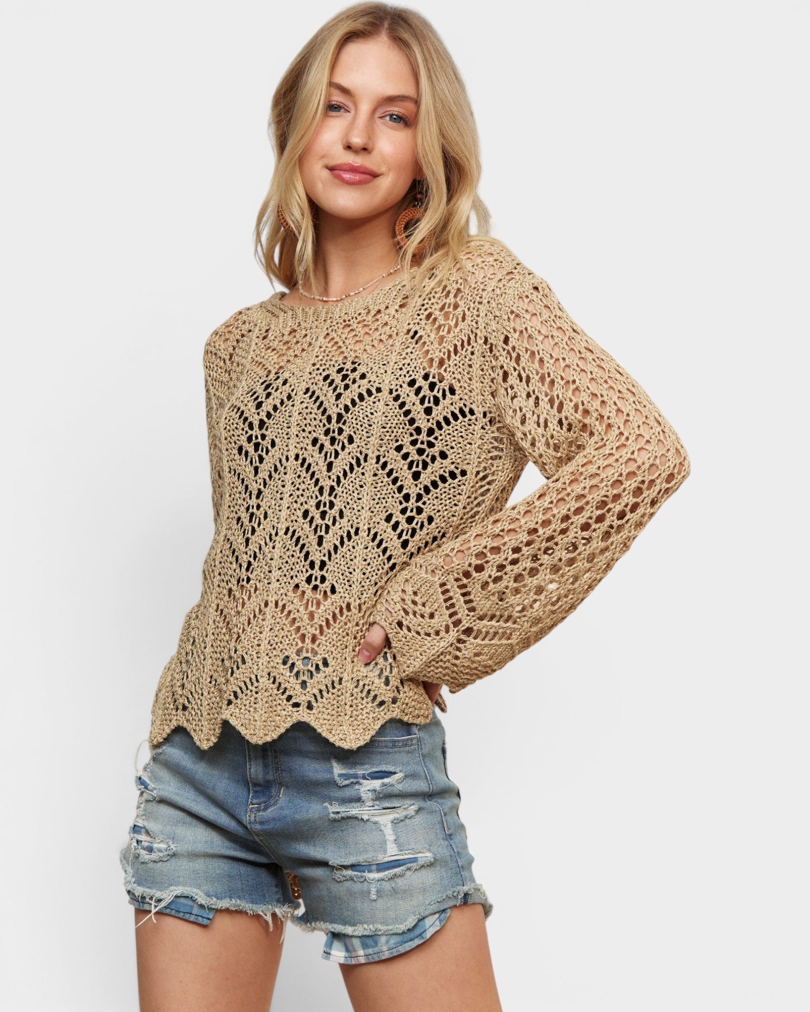 Woman wearing a beige crochet sweater and denim shorts on a white background