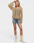 Woman wearing a beige crochet sweater, denim shorts, and white boots on a light background