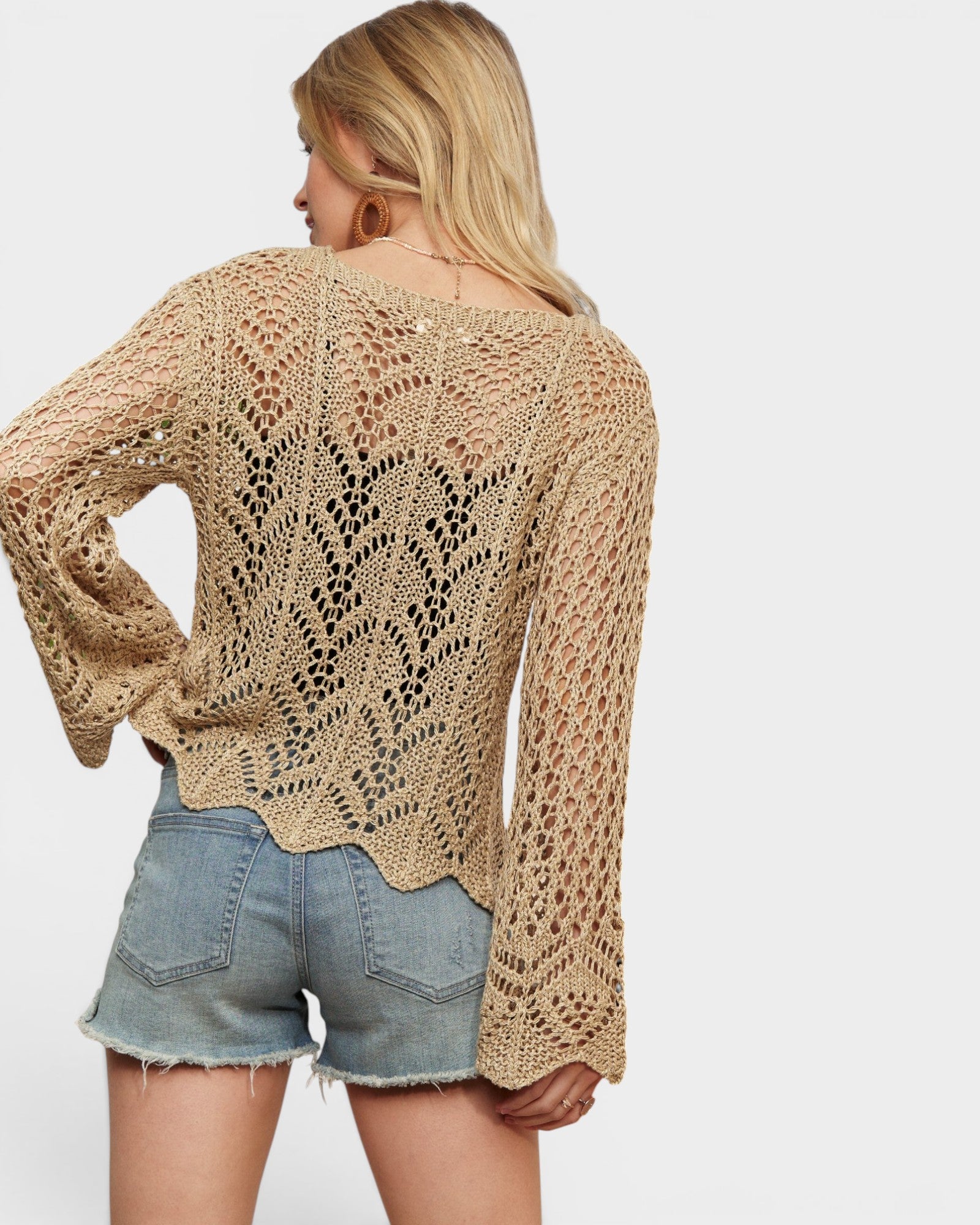Woman wearing a beige crochet top and denim shorts on a white background