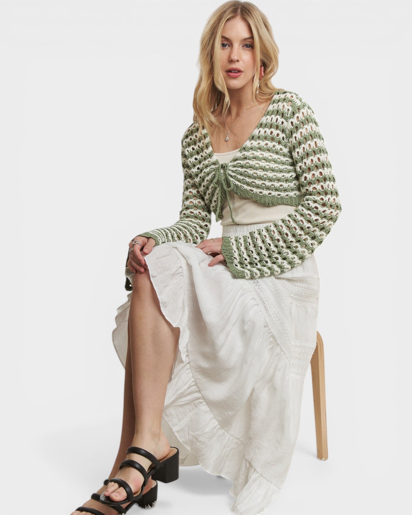 Woman wearing a green knitted cardigan over a white dress on a white background