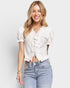 Woman wearing a white blouse with ruffle details and light blue jeans on a plain background