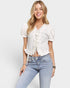 Woman wearing a white blouse with ruffle details and light blue jeans on a plain background