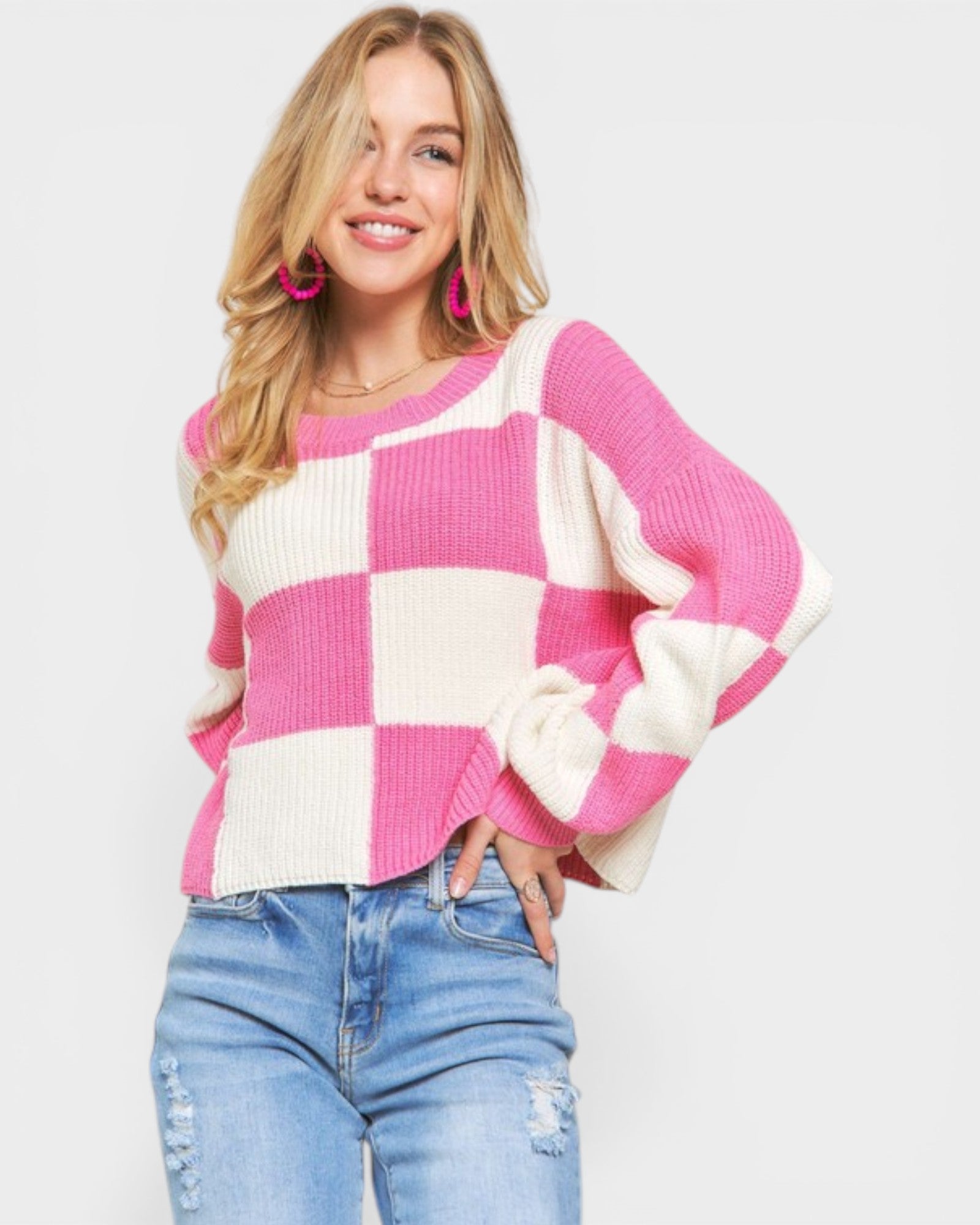 Woman wearing a pink and white checkered sweater with blue jeans on a light gray background