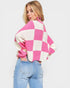 Woman wearing a pink and white checkered sweater with blue jeans on a plain background