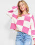Woman wearing a pink and white checkered sweater with blue jeans on a light gray background