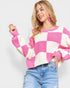 Woman wearing a pink and white checkered sweater with blue jeans on a light gray background