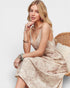 Woman in a beige dress sitting on a wicker chair against a white background