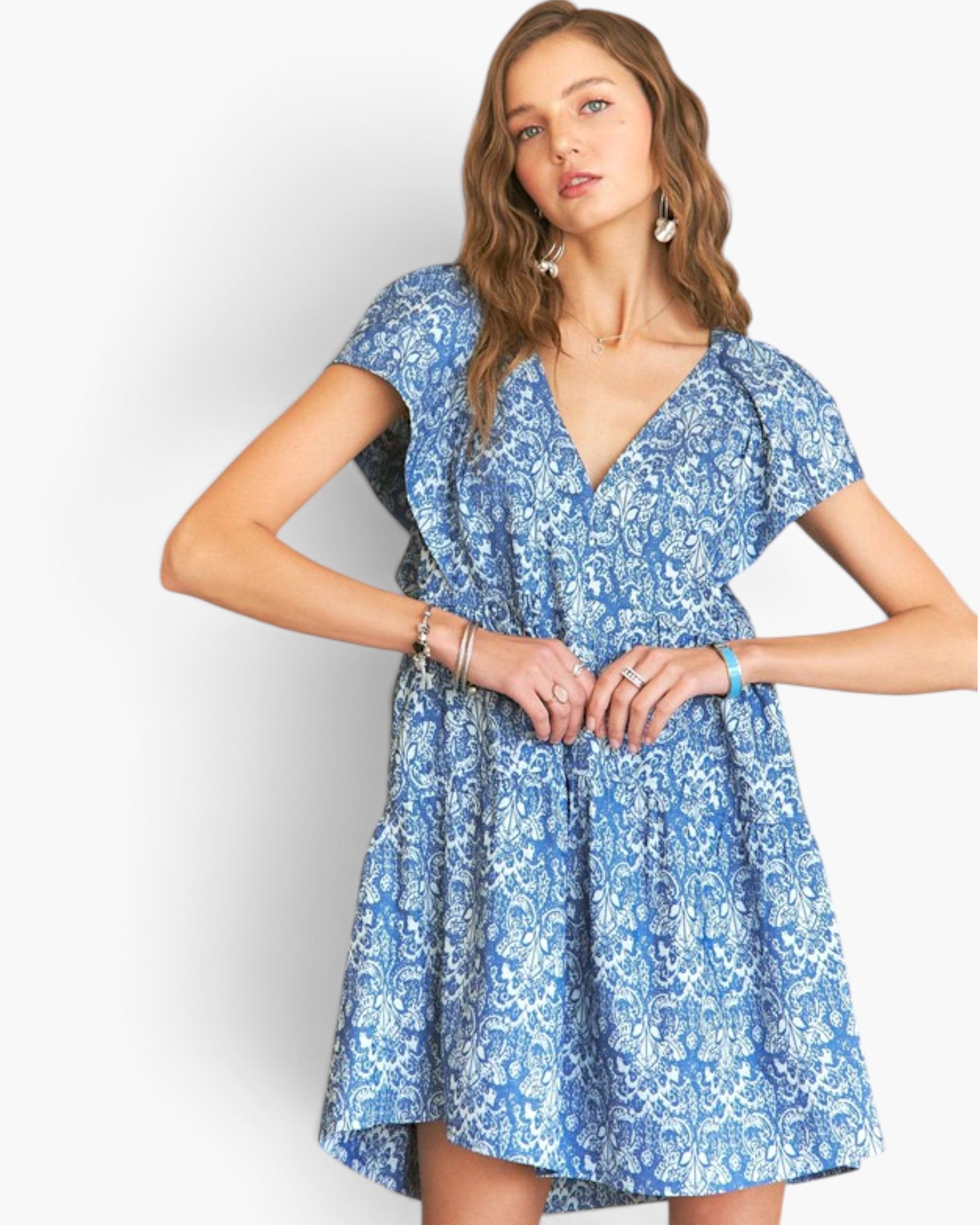 A woman modeling a short-sleeve blue and white floral print dress with a V-neckline and flared skirt against a plain light gray studio background.