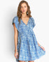 A woman modeling a short-sleeve blue and white floral print dress with a V-neckline and flared skirt against a light gray studio background.