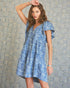 Woman wearing a blue floral dress against a textured wall.